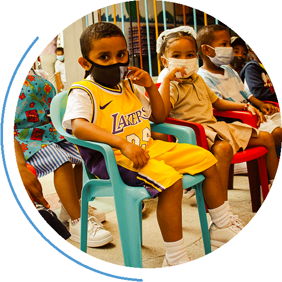 Kinder mit Corona-Masken sitzen auf Plastikstühlen