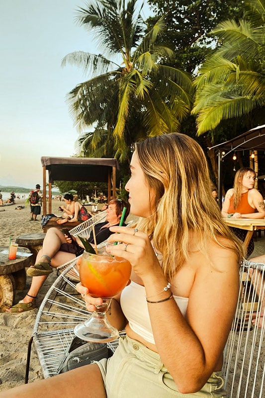 Liane sitzt in einer Strandbar und trinkt einen Cocktail