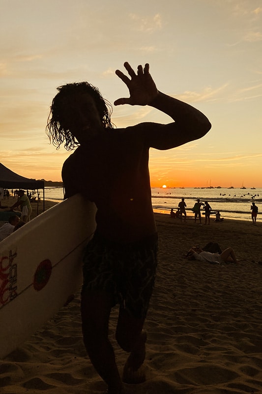 Surfer bei Sonnenuntergang winkt in die Kamera
