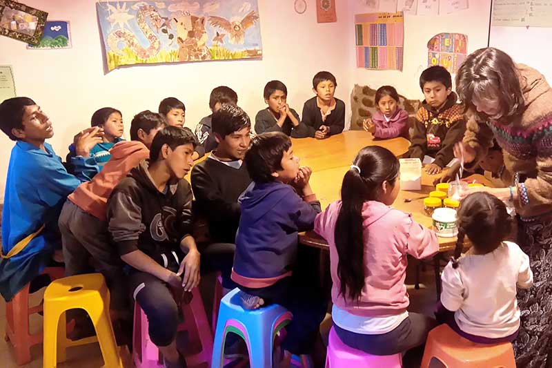 Gruppe peruanischer Kinder und Jugendlichen sitzt an rundem Tisch