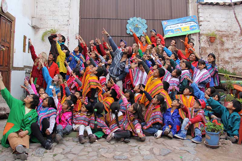 Group of volunteers with Peruvian children in traditional clothes pointing upwards