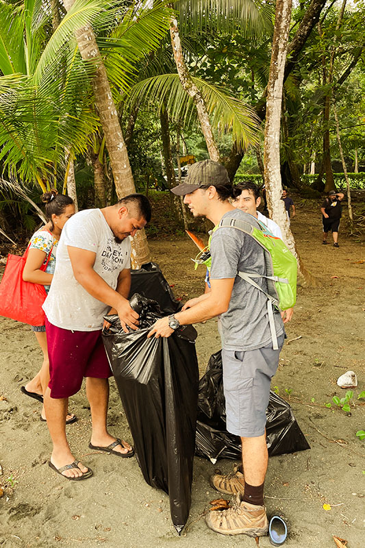 Männer sammeln Müll am Strand mit Palmen im Hintergrund