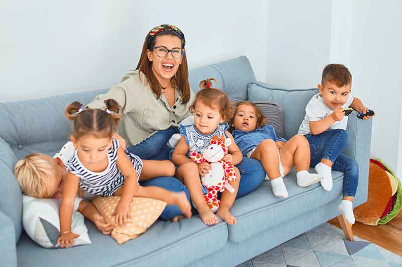 AuPair sitzt mit Kindern auf der Couch und lacht