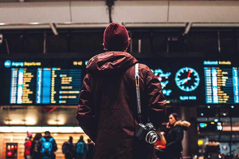 Mann mit Kamera vor Anzeigetafel am Flughafen
