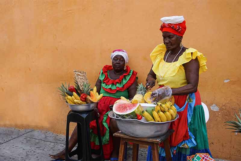 Frauen mit bunten Gewändern verkaufen Obst