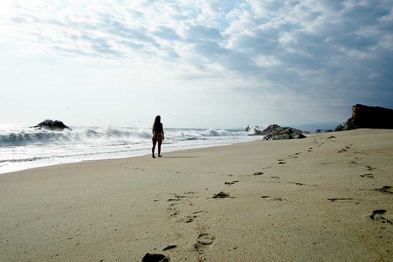 Woman walking on sandy beach with high waves in Mexico