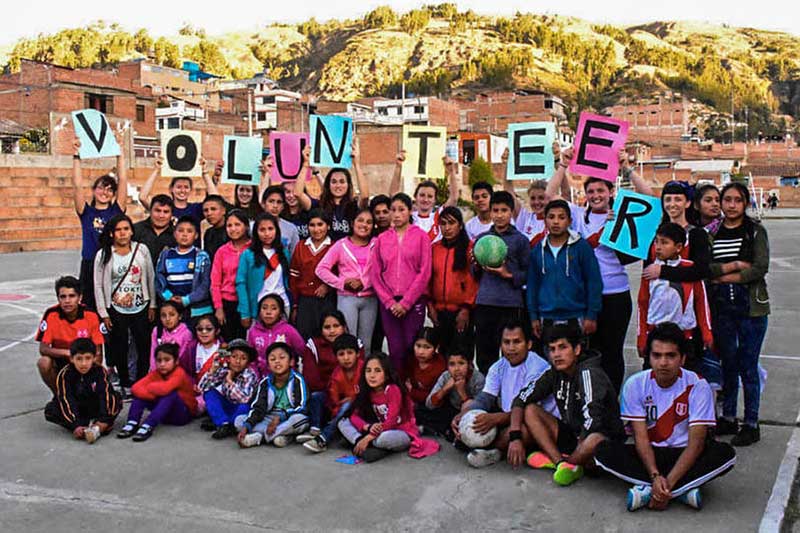 Gruppe peruanischer Kinder auf Sportplatz mit Bällen und Volunteer