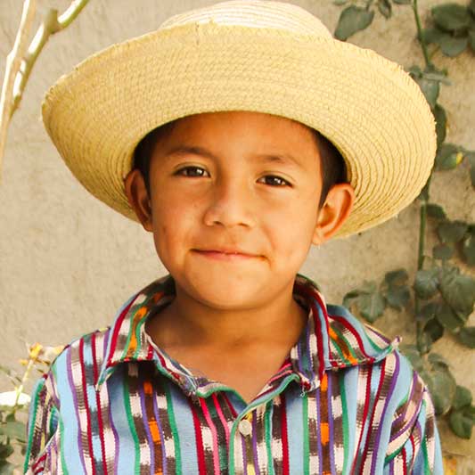 Einheimischer Junge mit Hut lächelt in die Kamera im Youth Development Projekt in Antigua in Guatemala